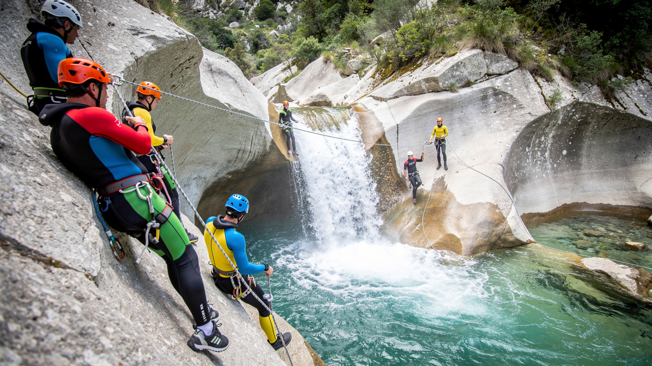 Groupe d’hommes et de femmes en combinaisons néoprène et casques descendant en rappel près d’une cascade dans le canyon de Purcaraccia, sur un granite clair.